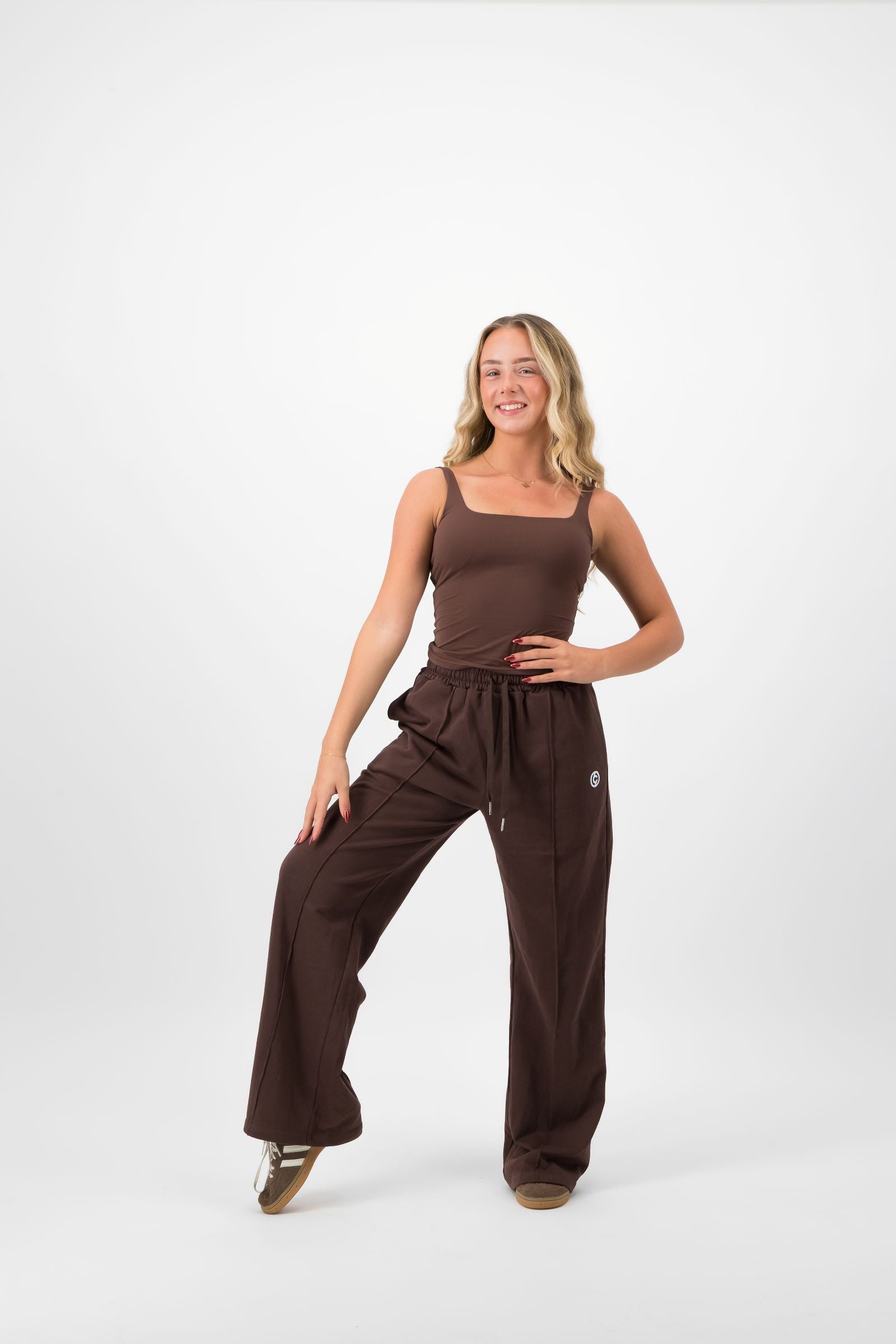 Woman wearing a brown sleeveless top and wide-leg pants on a white background