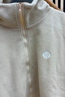 Close-up of a light beige fleece zip-up hoodie with a small circular logo on the chest, hanging on a wooden hanger.