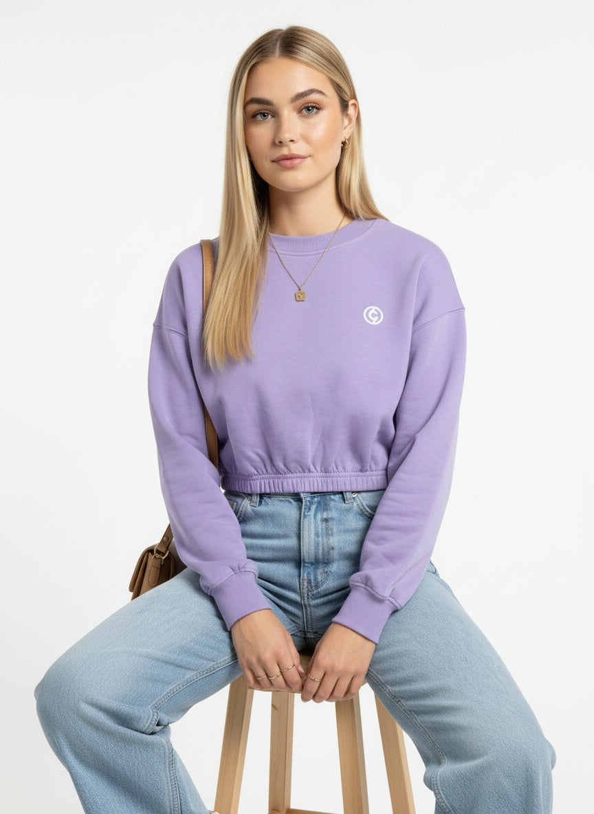 Person wearing a purple sweater with a logo, sitting on a stool against a white background