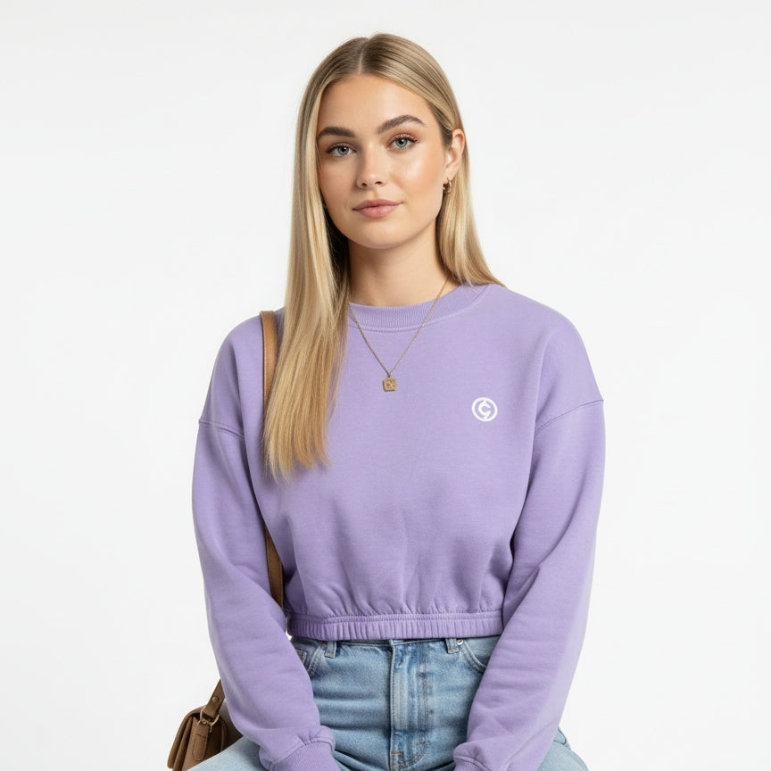 Person wearing a purple sweater with a logo, sitting on a stool against a white background