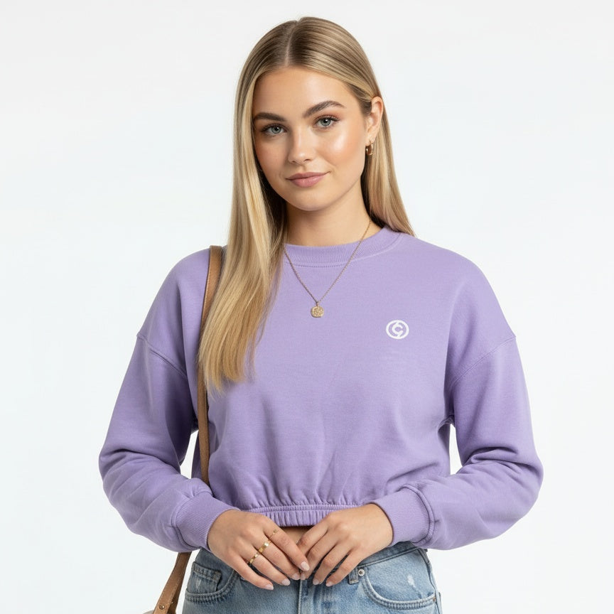 Woman wearing a purple sweatshirt with a logo and light blue jeans, standing against a plain background.