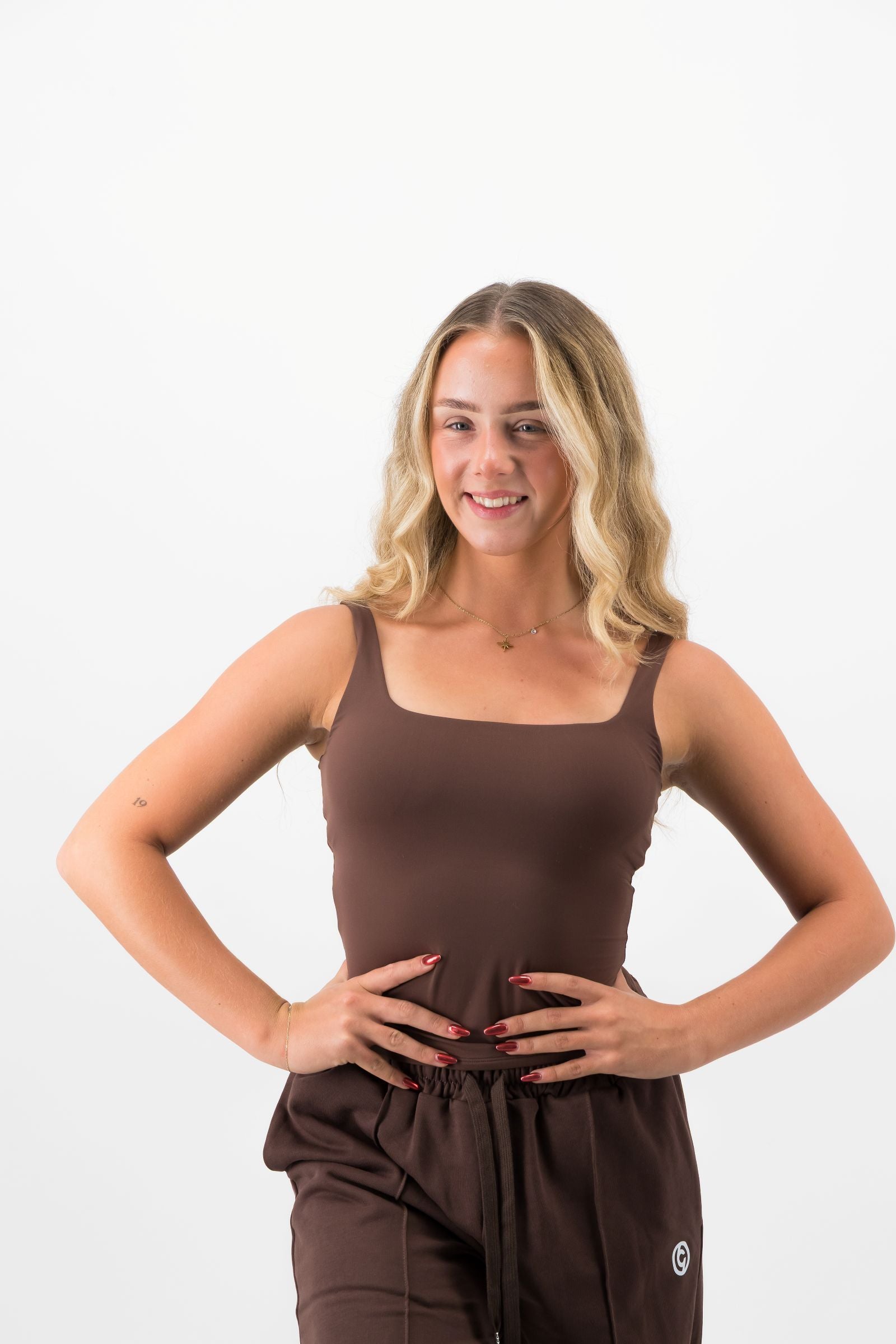 Woman wearing a brown tank top and pants on a white background