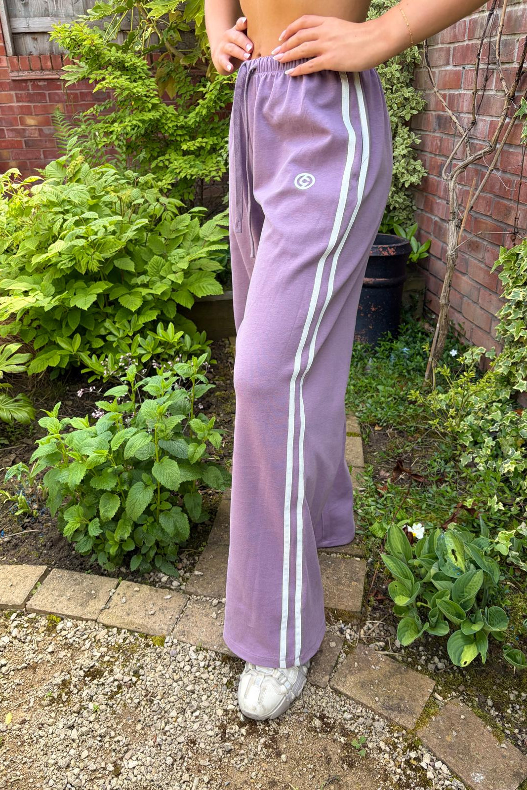 Person wearing lavender track pants with white stripes in a garden setting
