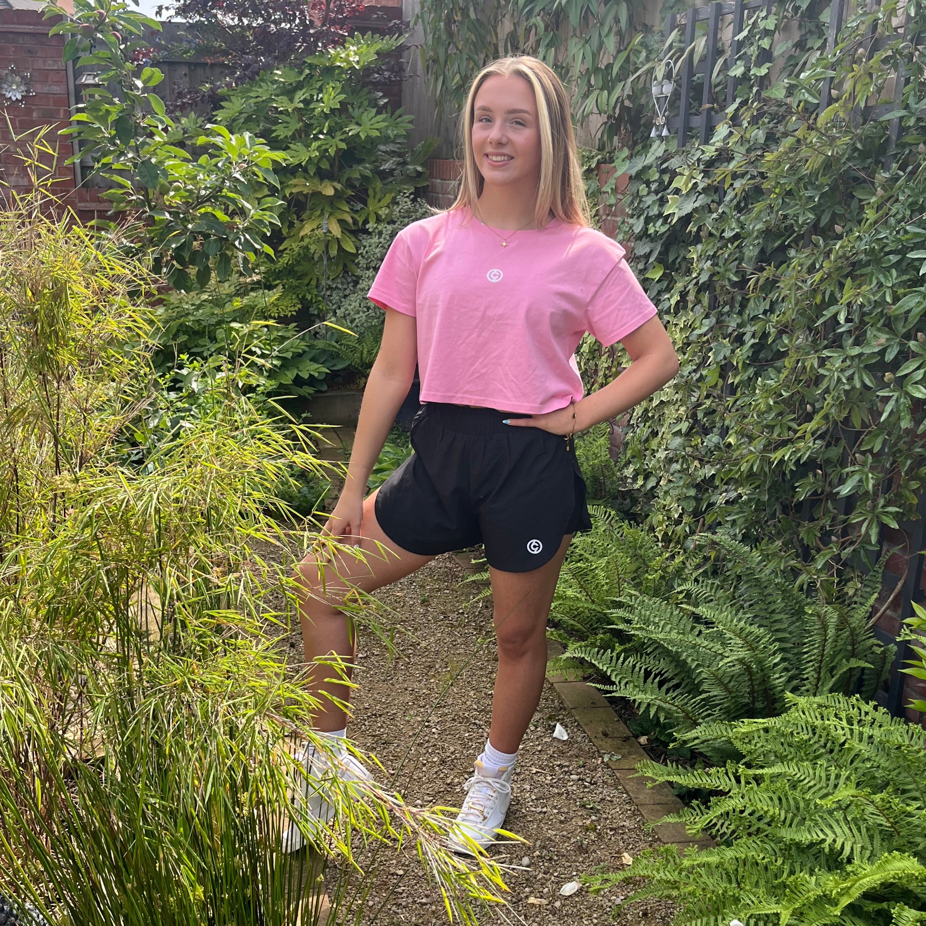 Woman in pink top and black skirt standing between stone columns in a sunlit stone building.
