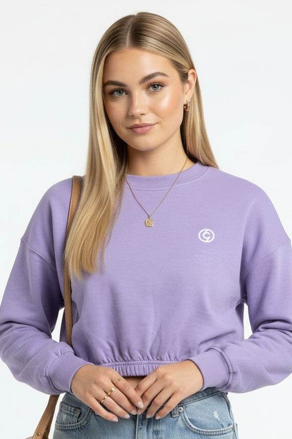 Woman wearing a purple sweatshirt with a logo and light blue jeans, standing against a plain background.