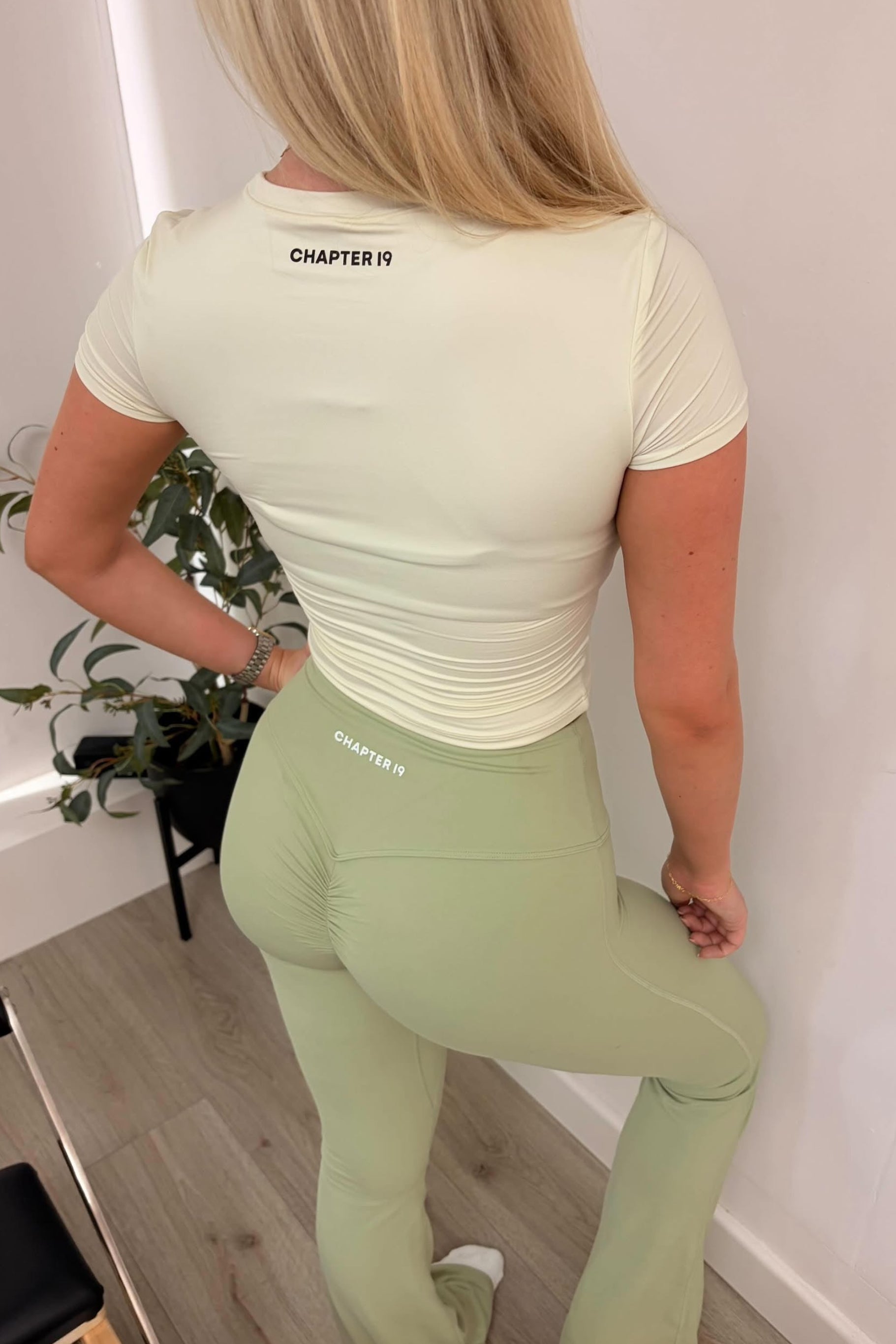 Person wearing a light green t-shirt and leggings with 'Chapter 19' branding, standing indoors.