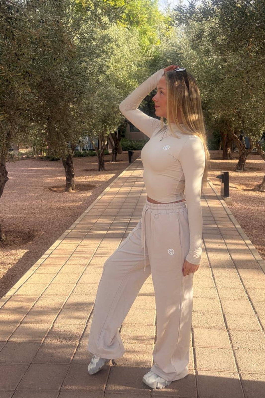 Woman in a beige outfit standing on a paved path with trees in the background