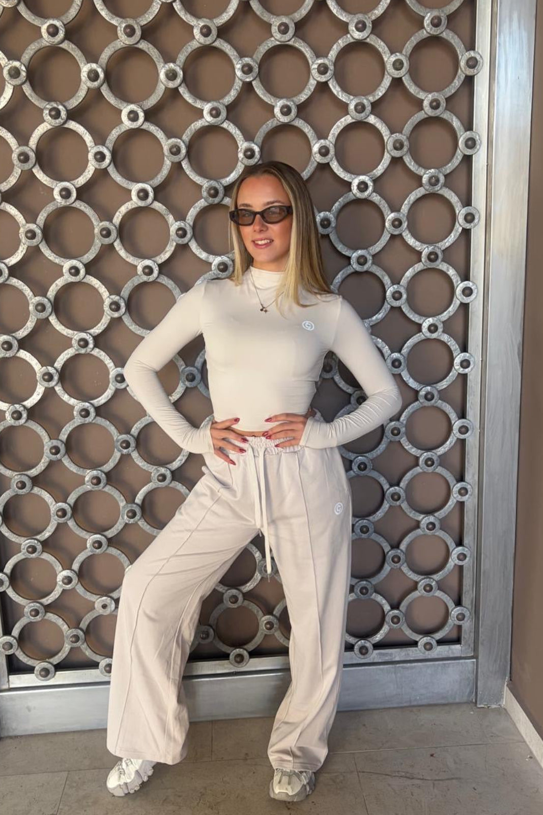 Person wearing a white outfit standing in front of a decorative wall.