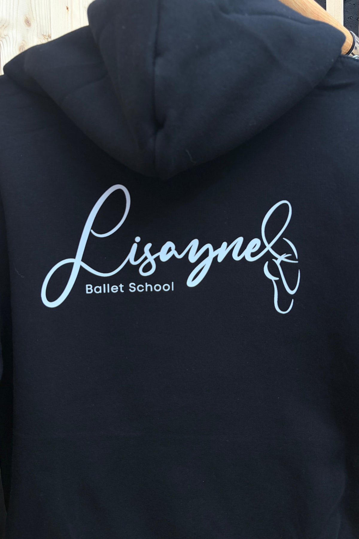 A black hoodie shown from the back, featuring a light blue script logo that reads 'Lisayne Ballet School' with a ballet shoe graphic.