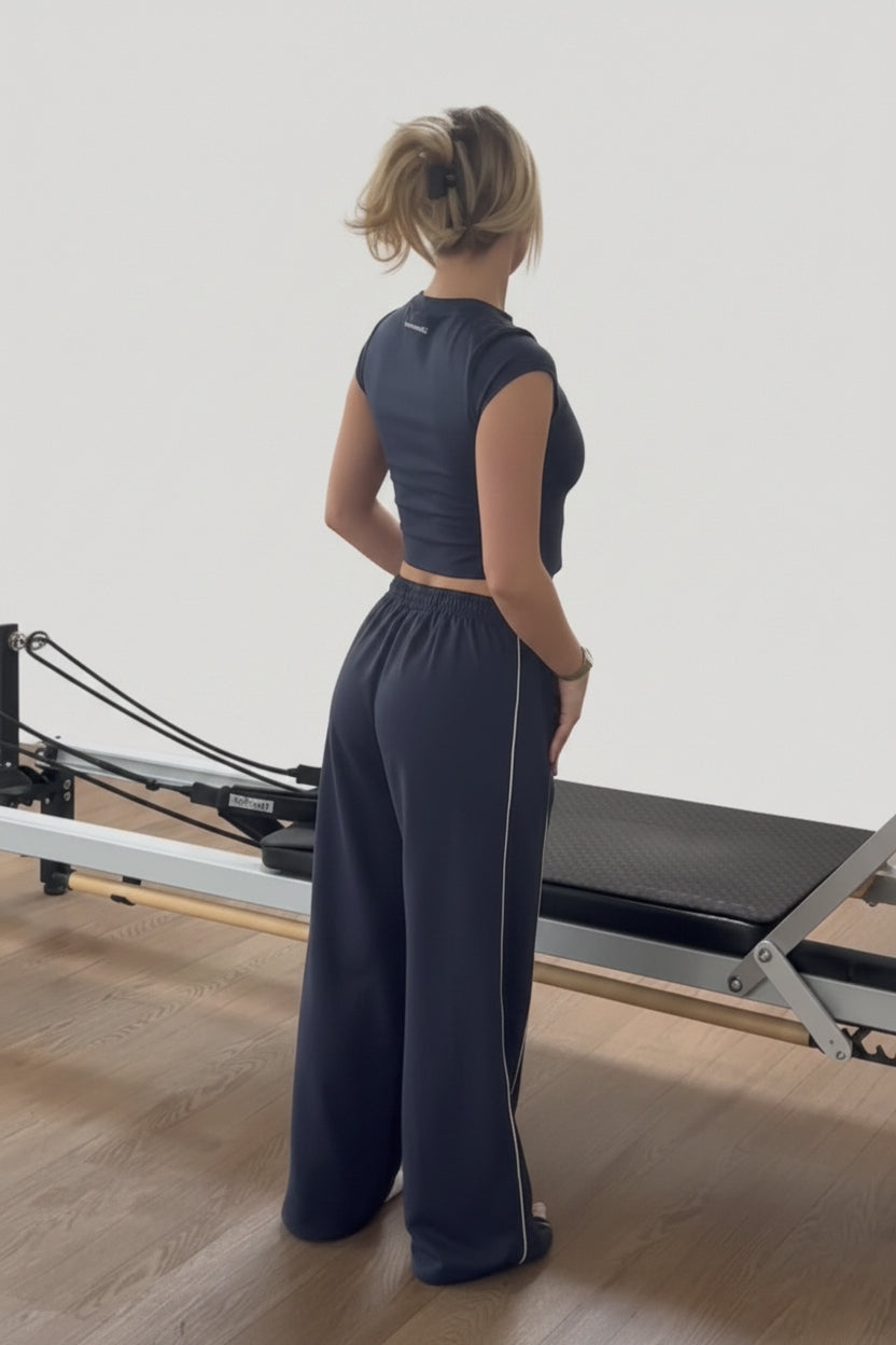 Woman standing in a Pilates reformer room with mirrors on the wall.